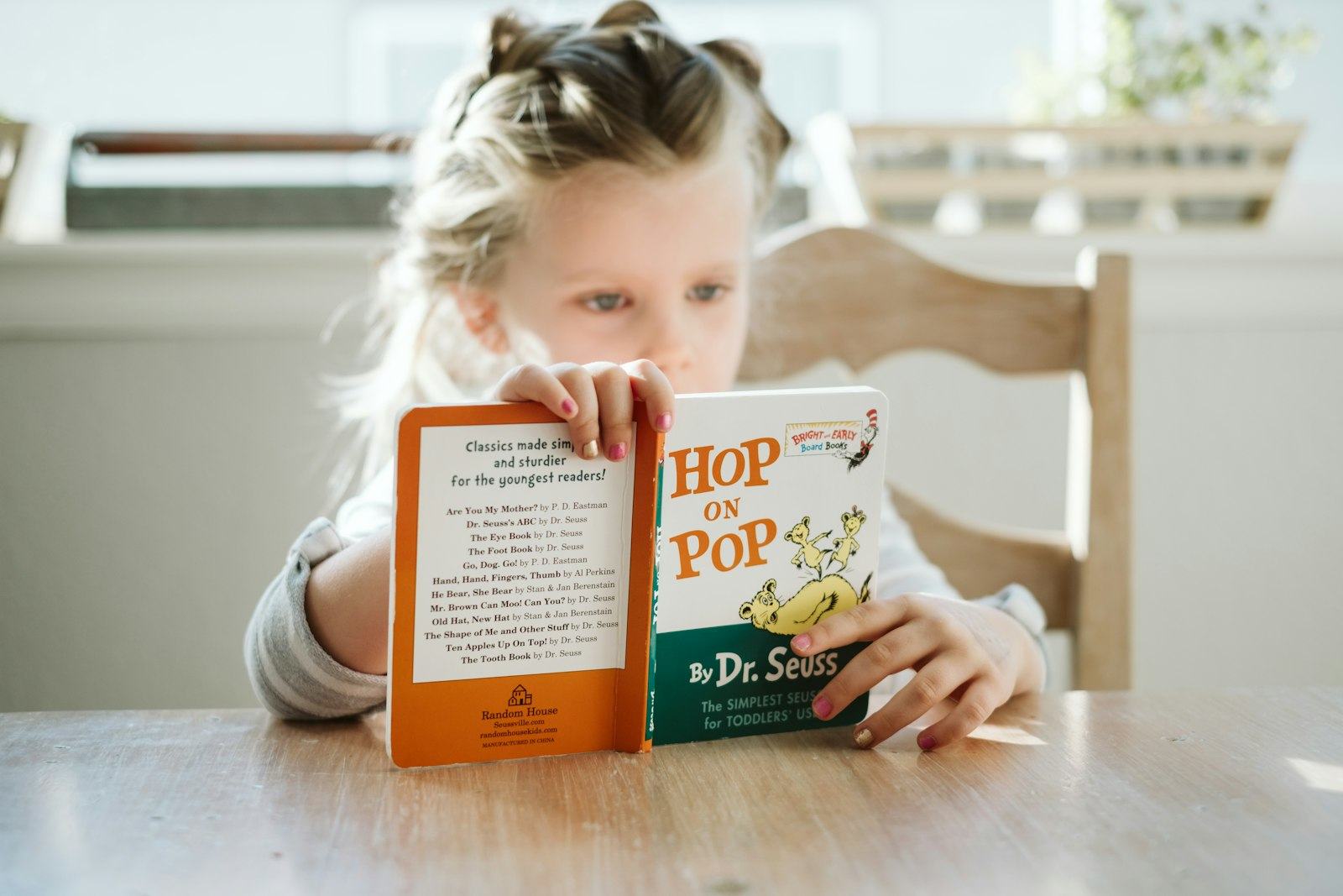 A young girl holds up a picture book and reads it closely.