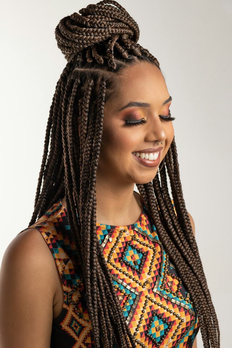 A smiling woman with long knotless braids gathered into a high bun, wearing a colourful patterned top