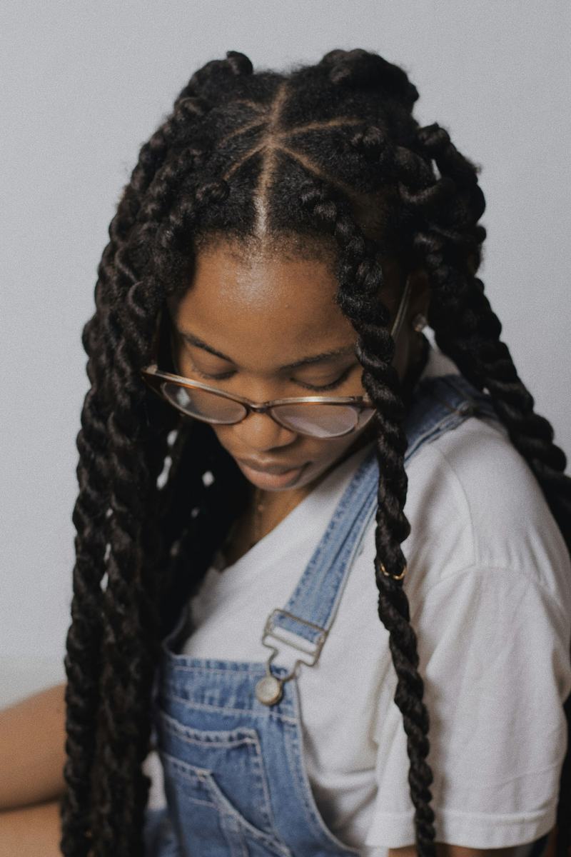 A young woman in denim overalls and glasses with long chunky box braids