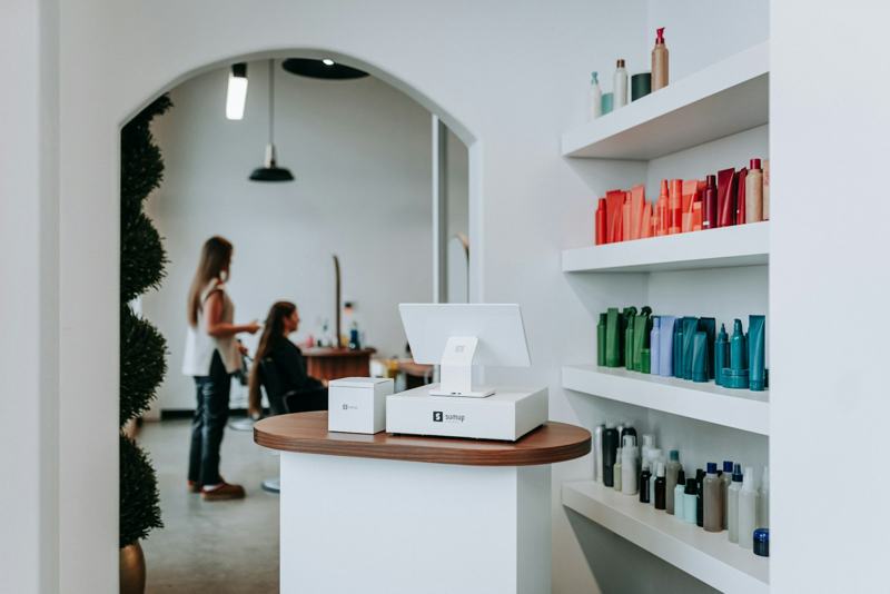 The bright studio, with an arched doorway, a white reception counter and shelves of hair products