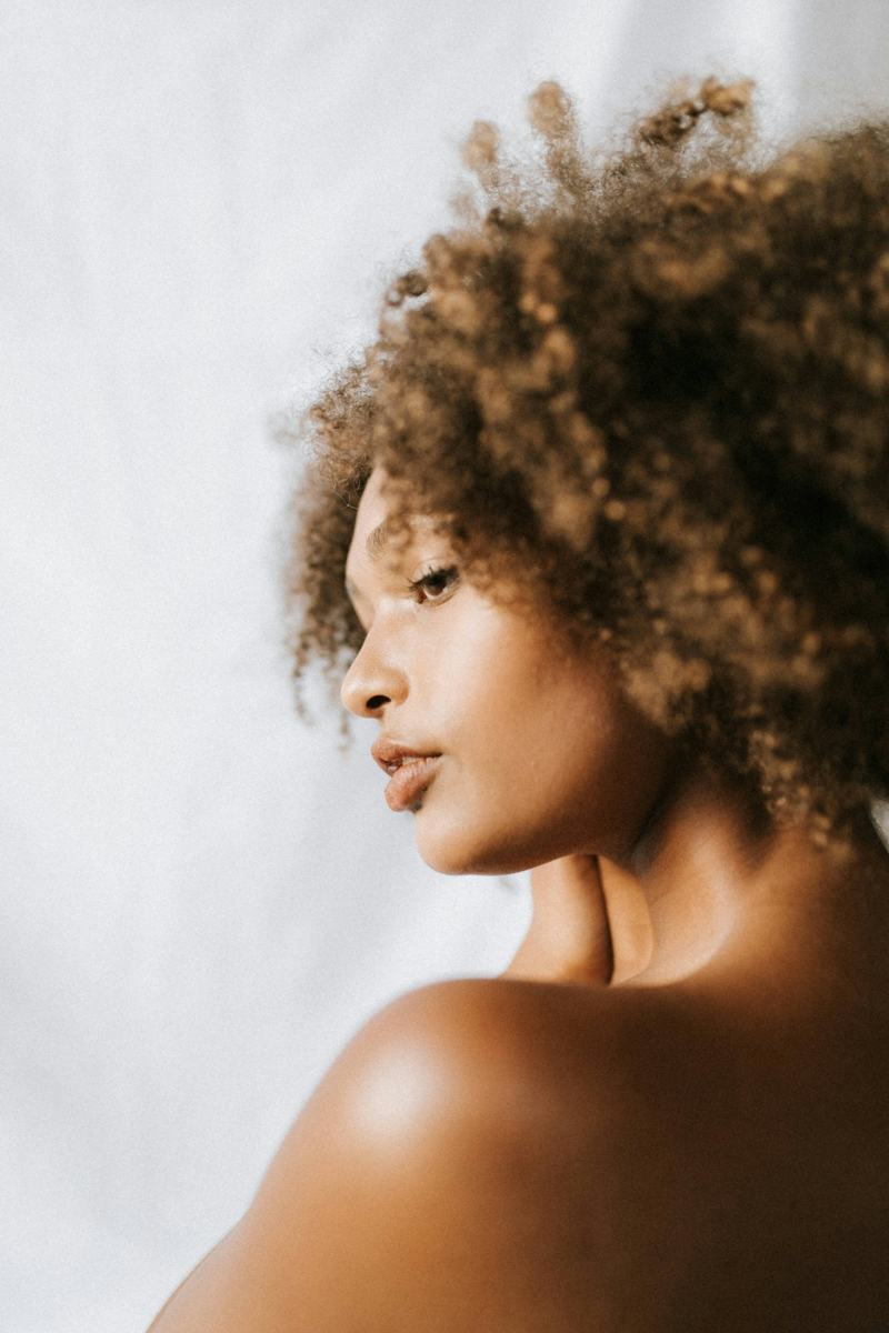 A woman in profile with a soft, defined curly afro against a pale backdrop