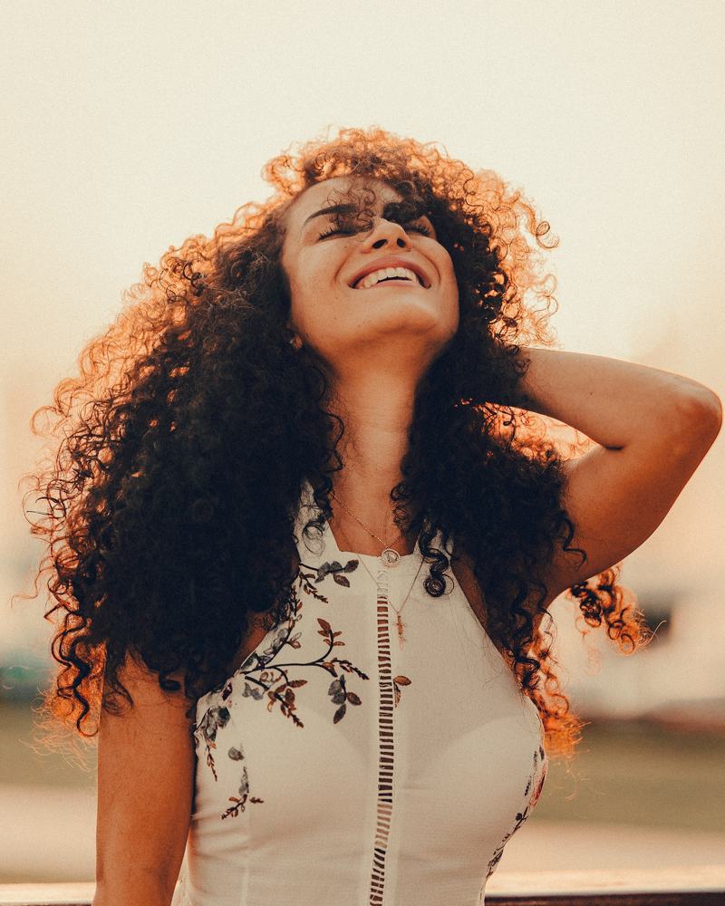 A woman laughing with her head tilted back, big natural curls catching the sun