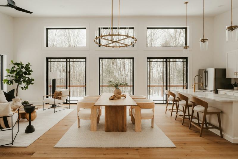 A bright, open living and dining room with tall windows and a wooden table