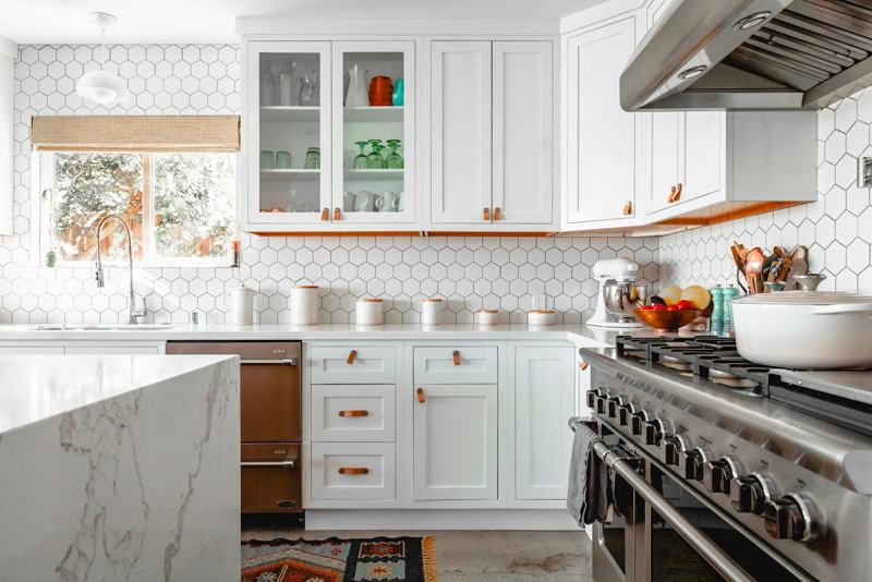 A spotless white kitchen with marble counters and a range