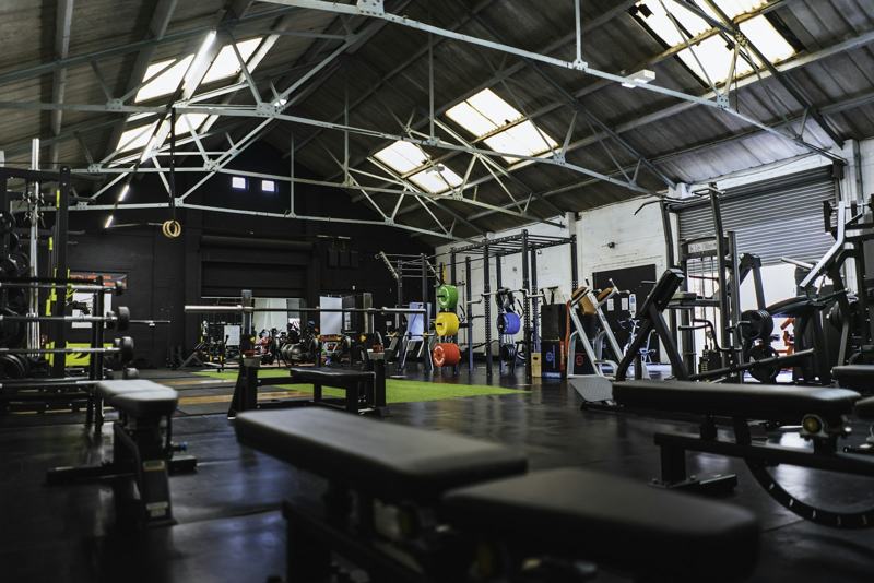 Wide view of an industrial gym floor with racks, benches and skylights