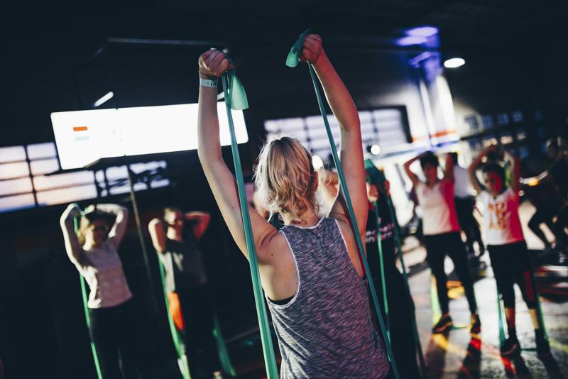 A group class works with resistance bands held overhead