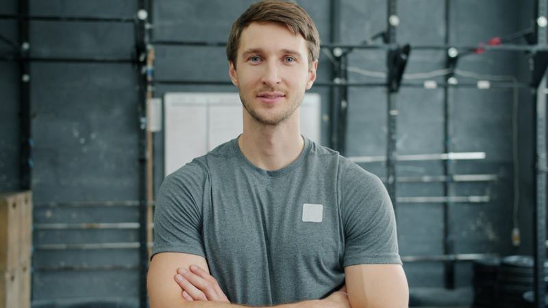 Head coach Marcus Cole standing with arms crossed in front of a squat rack