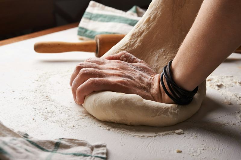 Hands kneading a mound of dough on a floured wooden counter