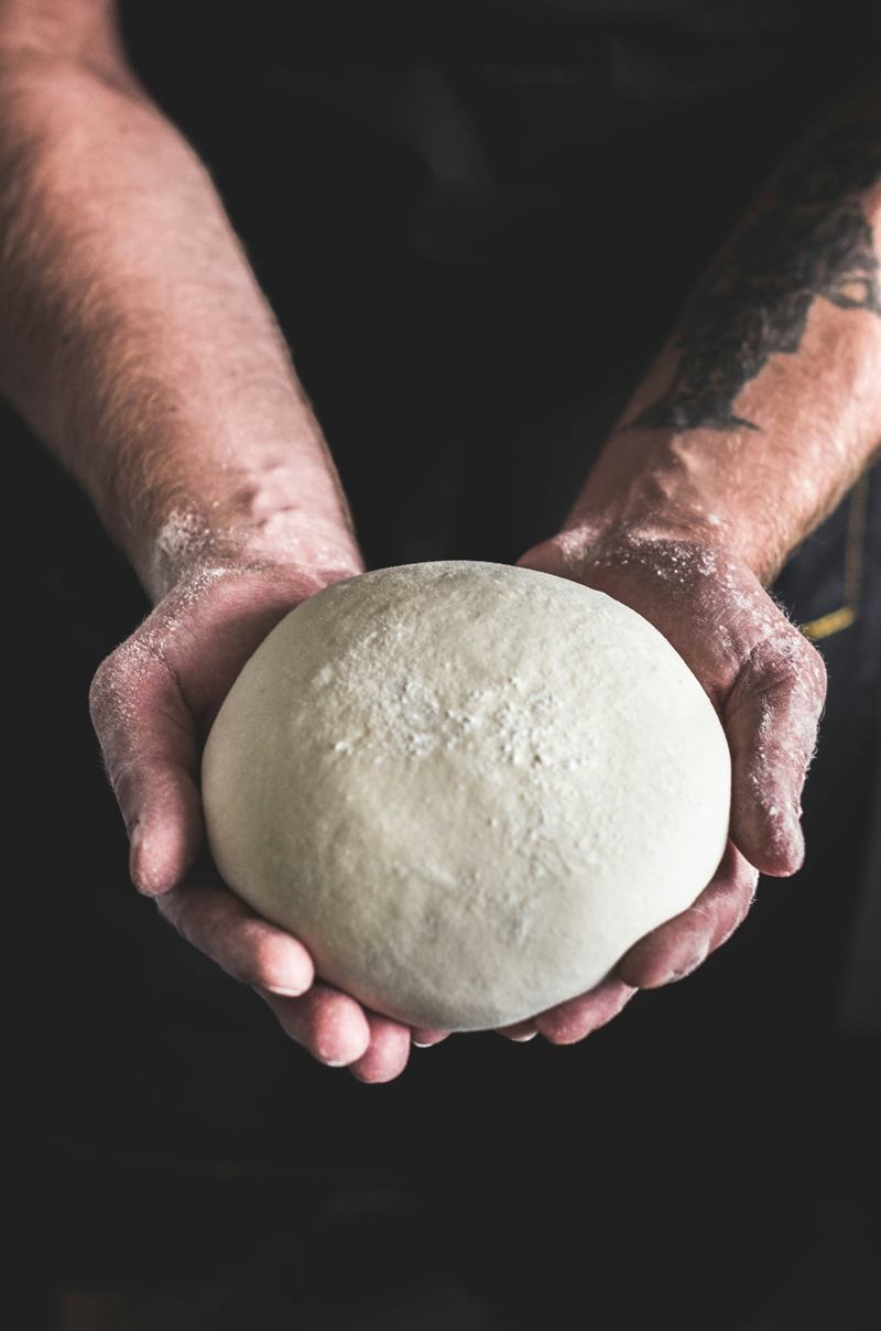A baker’s floury hands holding a smooth, round ball of dough