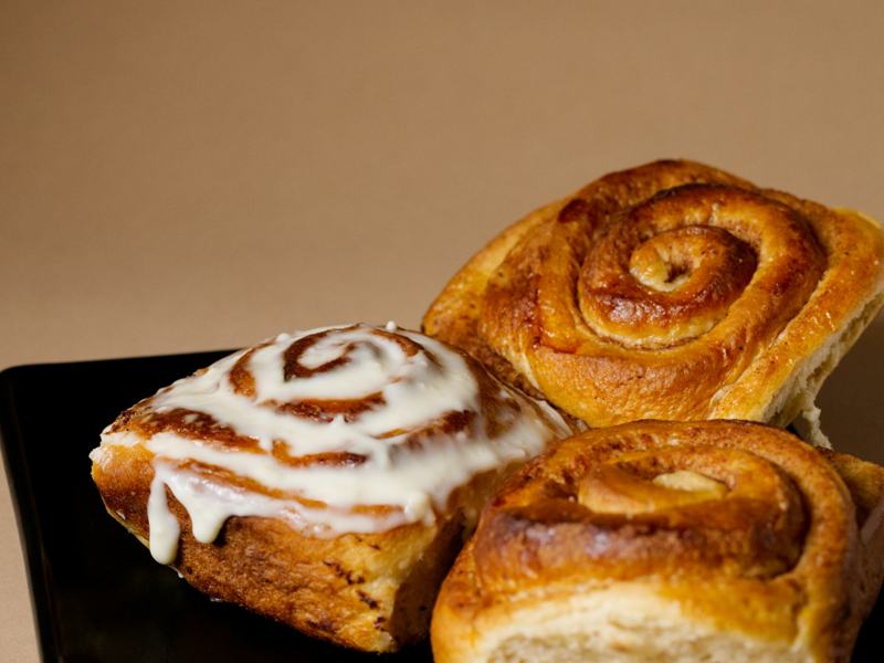 Close-up of cinnamon rolls, one dripping with white glaze