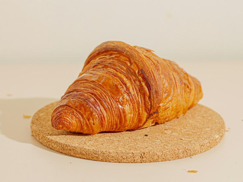 A single golden croissant resting on a round cork board