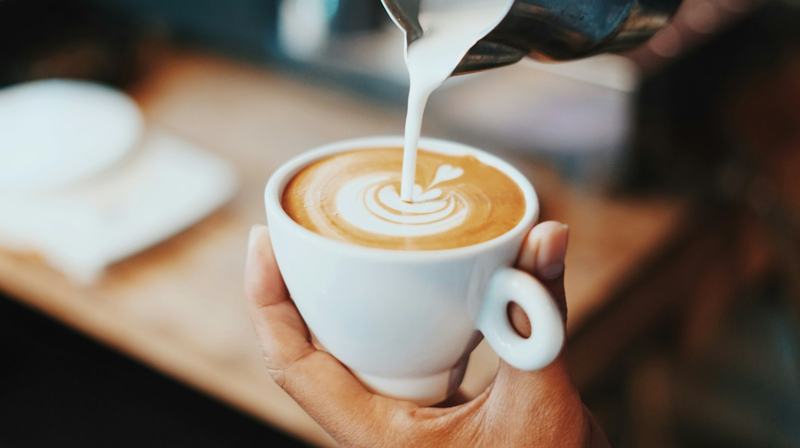 Steamed milk being poured into a latte, forming a leaf pattern