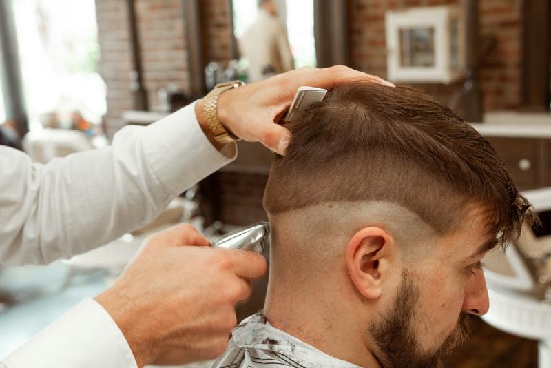 Barber blending a high fade with clippers while holding the top back with a comb