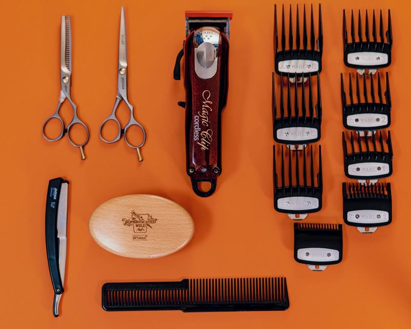 Clippers, shears and combs laid out on an orange surface