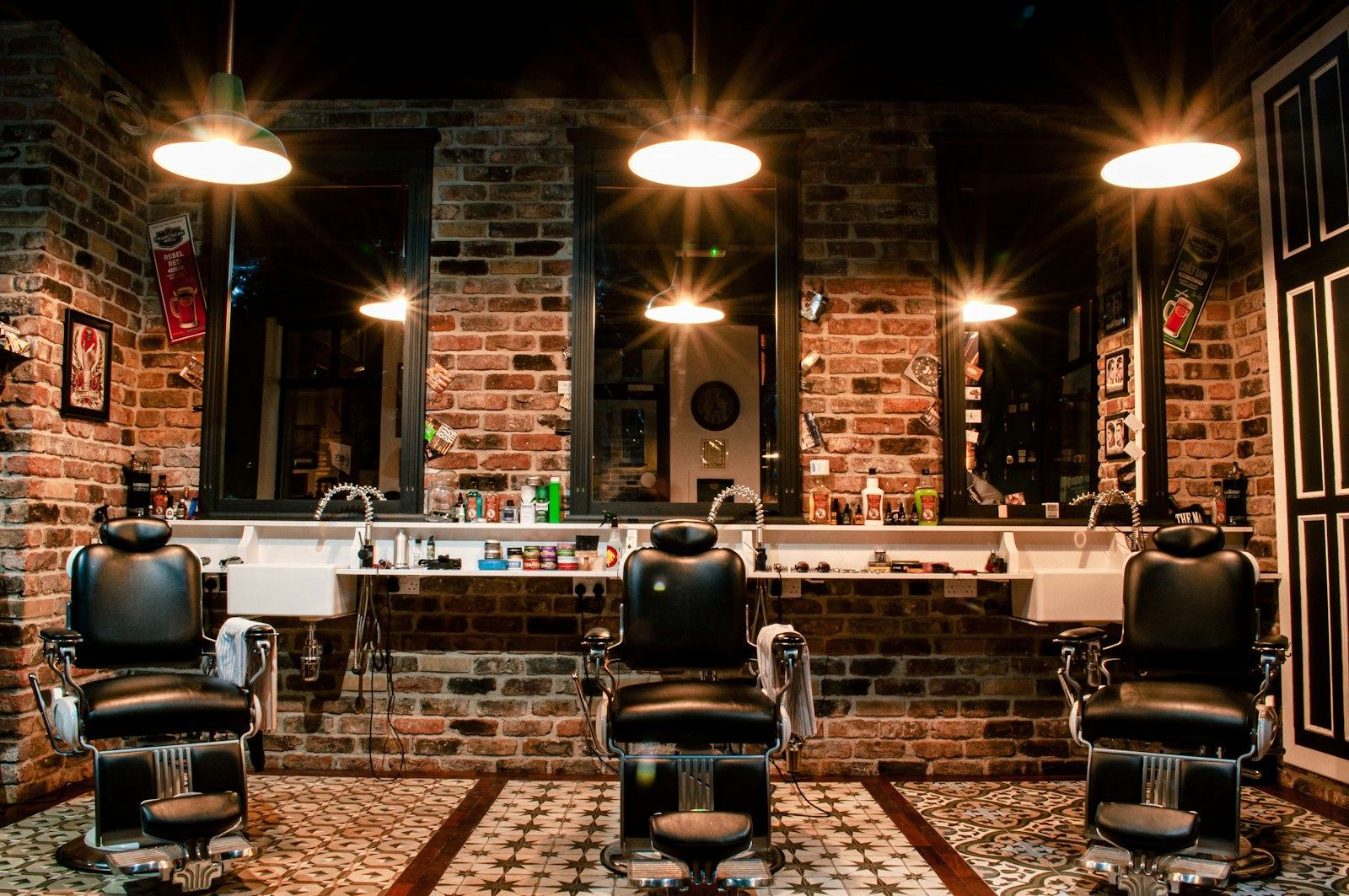 Inside Sharp & Co.: three black leather barber chairs under warm pendant lamps against an exposed brick wall